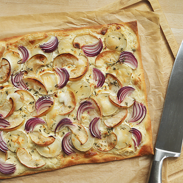 Apfel-Ziegenkäse-Flammkuchen mit einem Messer auf einem Holbrett